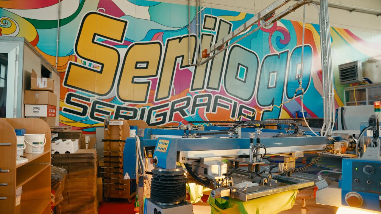 Carosello serigrafico nel laboratorio Serilogo, murale colorato sullo sfondo